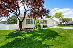 View of front facade featuring concrete driveway, fence, a front lawn, and an attached garage