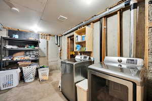 Clothes washing area featuring separate washer and dryer, laundry area, visible vents, and light colored carpet