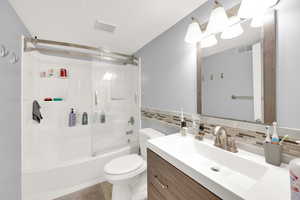 Full bath featuring toilet, enclosed tub / shower combo, visible vents, vanity, and decorative backsplash
