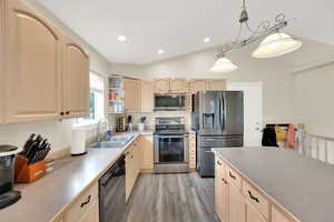 Kitchen featuring a sink, light wood-type flooring, pendant lighting, light brown cabinets, and appliances with stainless steel finishes