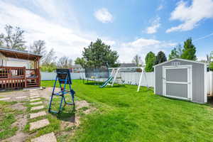 View of yard featuring a trampoline, a shed, a fenced backyard, a wooden deck, and a playground