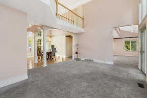 Carpeted living room featuring a chandelier, a towering ceiling, baseboards, and ornate columns