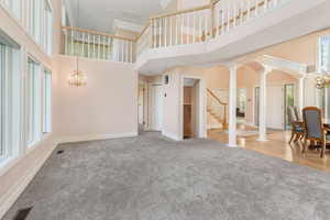Unfurnished living room featuring carpet, ornate columns, and a notable chandelier