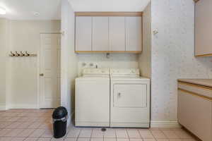 Laundry area with cabinet space, wallpapered walls, separate washer and dryer, baseboards, and light tile patterned flooring