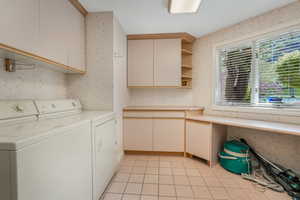 Laundry room with washing machine and clothes dryer, cabinet space, light tile patterned floors, and wallpapered walls