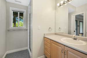 Bathroom featuring an enclosed shower, visible vents, baseboards, and vanity