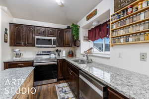 Kitchen featuring a sink, light stone counters, dark wood finished floors, dark brown cabinets, and appliances with stainless steel finishes
