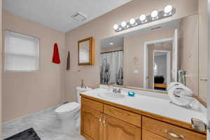 Full bath with marble finish floor, vanity, toilet, and visible vents