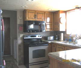 Kitchen featuring brown cabinetry, a sink, black microwave, stainless steel range with electric stovetop, and tasteful backsplash