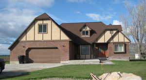 English style home featuring concrete driveway, a front yard, brick siding, a garage, and stucco siding