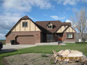 Tudor home featuring a garage, brick siding, driveway, and a front yard