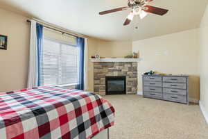 Carpeted bedroom featuring baseboards, a fireplace, and a ceiling fan