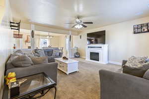 Living room featuring baseboards, carpet flooring, a glass covered fireplace, and ceiling fan with notable chandelier