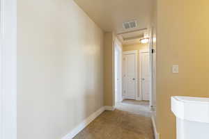Hall with baseboards, attic access, visible vents, and light colored carpet