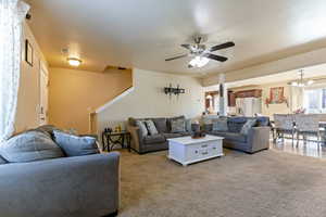 Living area featuring visible vents, light colored carpet, and ceiling fan with notable chandelier