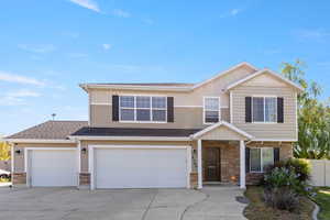 View of front of home with stone siding, an attached garage, driveway, and fence