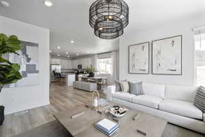 Living room featuring a notable chandelier, light wood-style flooring, recessed lighting, baseboards, and visible vents