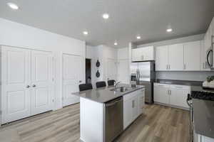 Kitchen with a sink, light wood-type flooring, an island with sink, and appliances with stainless steel finishes