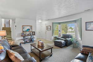 Living area featuring baseboards, carpet flooring, visible vents, and stairway