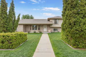 Split level home featuring a front yard, roof with shingles, and brick siding