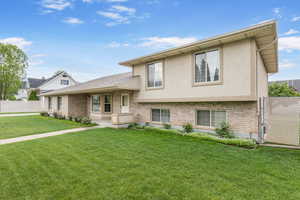 Tri-level home with brick siding, stucco siding, fence, and a front yard