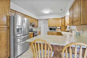 Kitchen with a sink, a peninsula, stainless steel appliances, under cabinet range hood, and light countertops