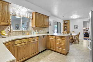 Kitchen featuring a sink, a peninsula, backsplash, light countertops, and appliances with stainless steel finishes