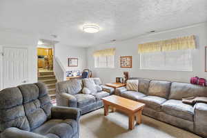 Carpeted living room featuring a textured ceiling, visible vents, and stairway
