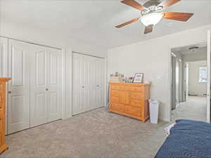 Bedroom with light colored carpet, a textured ceiling, a ceiling fan, and multiple closets