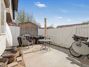 View of patio / terrace with a fenced backyard, a grill, a storage unit, and an outbuilding