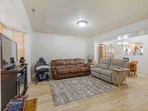 Living room with ornamental molding, visible vents, an inviting chandelier, and light wood-type flooring