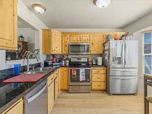 Kitchen featuring light wood finished floors, light brown cabinetry, a sink, dark countertops, and stainless steel appliances