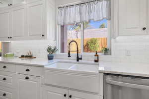 Kitchen with white cabinets, backsplash, stainless steel dishwasher, and a sink