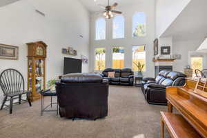 Living room featuring a towering ceiling, carpet flooring, a ceiling fan, and visible vents