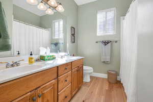Full bath with a sink, double vanity, toilet, and wood finished floors