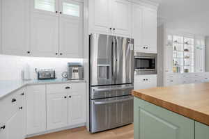 Kitchen featuring butcher block countertops, light wood finished floors, decorative backsplash, white cabinets, and appliances with stainless steel finishes