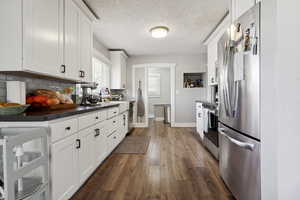 Kitchen featuring dark countertops, dark wood finished floors, white cabinetry, appliances with stainless steel finishes, and decorative backsplash