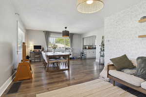 Living room with wood finished floors, wallpapered walls, a textured ceiling, visible vents, and baseboards
