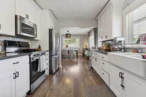 Kitchen with white cabinets, dark countertops, appliances with stainless steel finishes, and tasteful backsplash