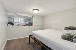 Bedroom with baseboards, dark carpet, visible vents, and a textured ceiling