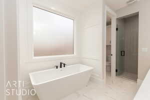 Full bath with toilet, a shower stall, a freestanding tub, marble look tile flooring, and baseboards