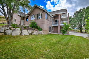 Rear view of house with brick siding, a lawn, and a balcony