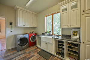 Laundry area featuring a sink, cabinet space, washing machine and clothes dryer, dark wood-style flooring, and baseboards