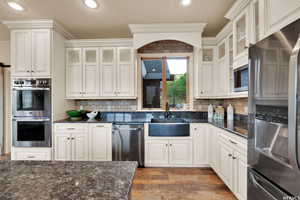 Kitchen featuring glass insert cabinets, a sink, decorative backsplash, wood finished floors, and appliances with stainless steel finishes