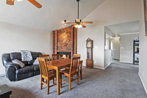 Carpeted dining space with baseboards, a fireplace, a ceiling fan, and high vaulted ceiling