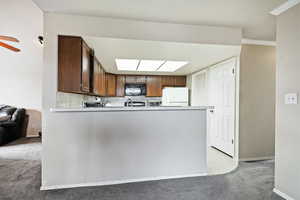 Kitchen featuring freestanding refrigerator, baseboards, black microwave, a peninsula, and light colored carpet