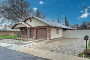 View of front facade with brick siding, fence, an attached garage, concrete driveway, and a gate