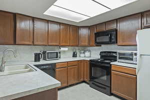 Kitchen with a toaster, a sink, backsplash, black appliances, and light countertops