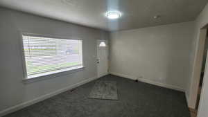 Foyer entrance featuring a textured ceiling, baseboards, visible vents, and dark carpet