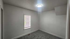 Spare room with visible vents, baseboards, and dark carpet